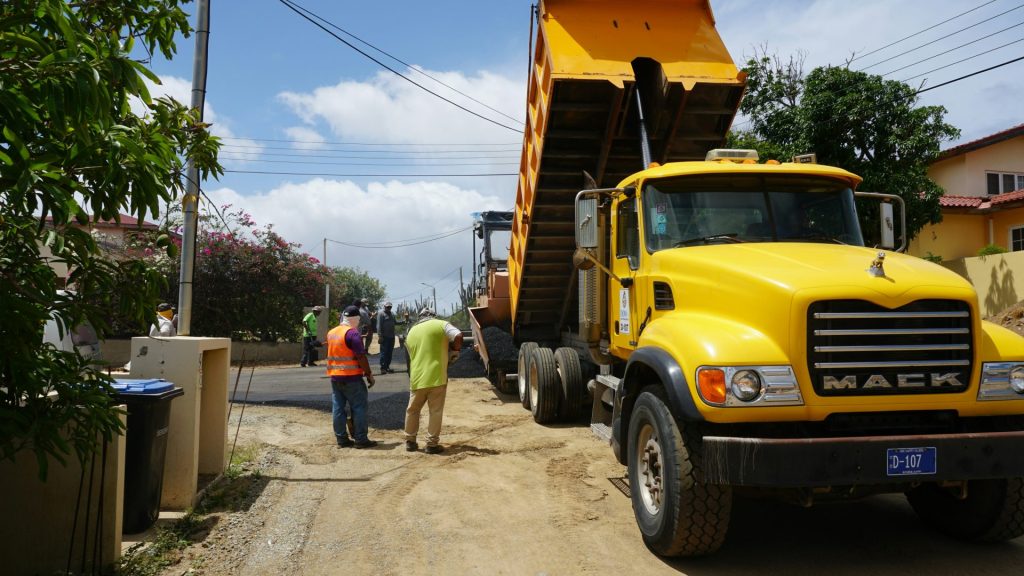 Yellow dump truck unloading dirt onto a street.